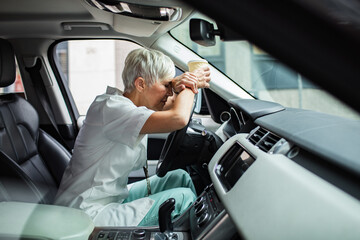 Stressed senior nurse sitting in her car during coffee break