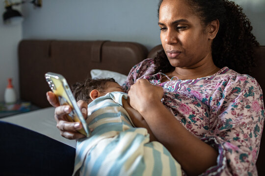 Mother breastfeeding while using smartphone at home