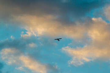 A lone airplane silhouetted against a vibrant evening sky, clouds tinged with gold and blue hues.