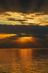Obraz premium A serene sunset casting a golden glow over calm sea waters, with rays piercing through clouds. Perfect for projects needing a peaceful and natural ambiance.