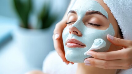 A serene woman with a towel headwrap enjoys a pampering session with a green face mask applied to her skin, lying back with eyes closed, depicting relaxation and self-care.