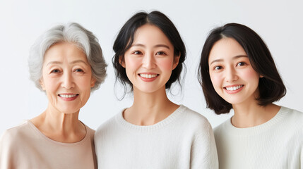Three generations of women smiling together in soft sweaters against a light background.