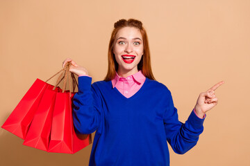 Portrait of pretty young lady indicate finger empty space shop bags wear blue sweater isolated on...
