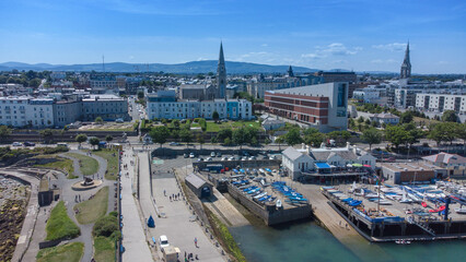 Fototapeta premium An aerial drone shot of Dun Laoghaire, Ireland, captures the picturesque coastal town from above. The image showcases the bustling harbor, with boats and ships anchored in the clear blue waters.