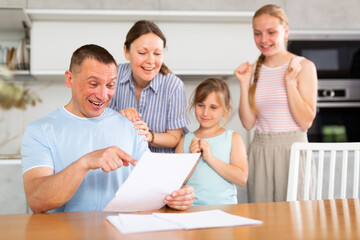 Joyful family gets acquainted, considers printed plan of future new apartment, housing. Wife claps hands, daughters happily hug father