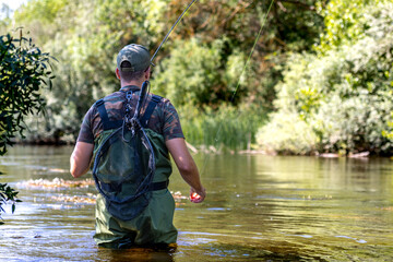 Man fly fishing in a river with fishing net on his back