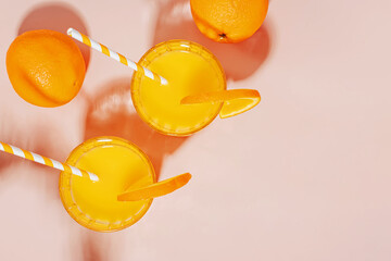 Two glasses of orange juice and oranges on a pastel pink b