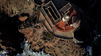 A lighthouse shines above the dark waters  its light cutting through the night and offering...