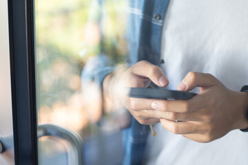 At school, using smartphone, asian teenage boy texting while standing by window