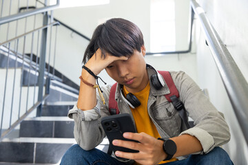 At school, Sitting on stairs, asian teenage boy with headphones using smartphone, looking stressed