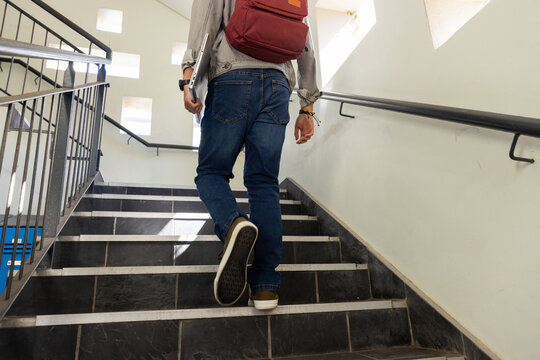 Walking up stairs, asian teenage boy with red backpack heading to class in school