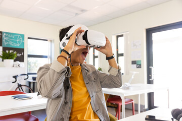 Using VR headset, excited asian teenage boy experiencing virtual reality in school classroom