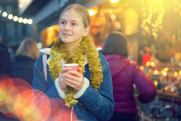 Happy teenagers girl holding hot cup of coffee in hands at street christmas fair