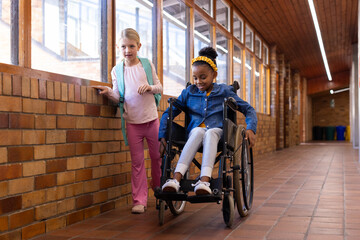 In school hallway, african american girl in wheelchair with female friend both smiling and talking