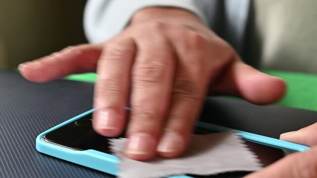Unrecognizable woman uses a special soft screen cloth to wipe dust spots from a mobile phone before installing an anti-scratch screen protector.