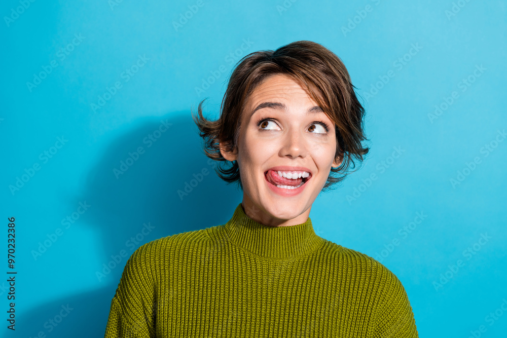 Poster Photo of cheerful adorable girl wear trendy khaki clothes lick her teeth look up empty space isolated on cyan color background