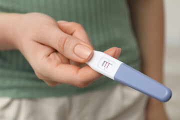 Fototapeta premium Woman holding positive pregnancy test indoors, closeup view