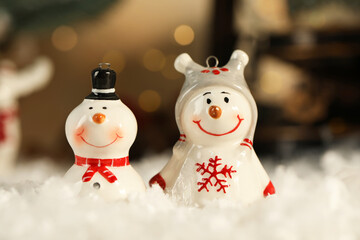 Funny snowman figures on artificial snow against blurred lights, closeup