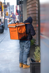 Food courier driver with food delivery sign on the cooler backpack waiting in front of a restaurant...