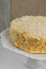 Cake Napoleon with crispy layers, covered in crumbs, standing on a white decorative stand.