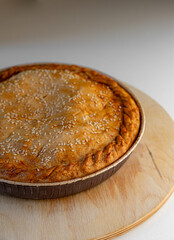 Pie with a golden crust and sesame seeds, resting on a wooden stand.