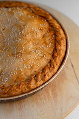 Pie with a golden crust and sesame seeds, resting on a wooden stand.