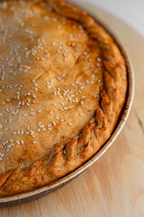 Pie with a golden crust and sesame seeds, resting on a wooden stand.
