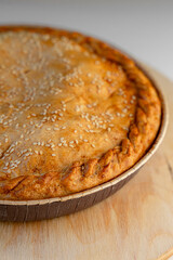 Pie with a golden crust and sesame seeds, resting on a wooden stand.