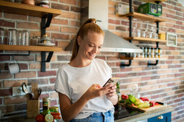 Smiling young woman using smartphone in modern kitchen