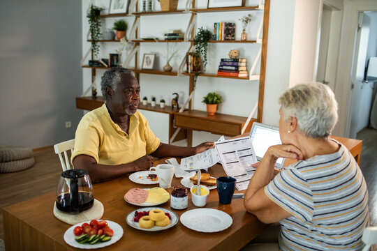 Diverse senior couple going over financials with laptop during breakfast