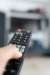 Hand Holding TV Remote Pointing at Blurred TV in Background