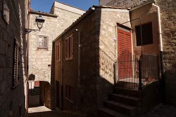 Charming narrow alleyway in Petralia Soprana, Sicily, featuring rustic stone buildings, wooden shutters, and the interplay of light and shadow on a sunny day