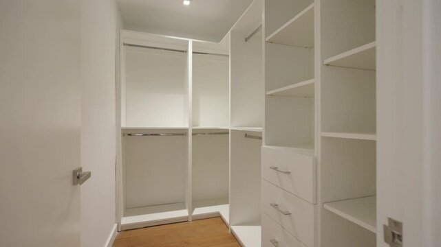 Well-lighted wardrobe with open doors, revealing shelves, drawers and hanging space. White and organized cabinet with clean and minimalist design