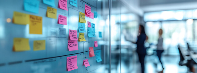 Fototapeta premium A vibrant shot of transparent board filled with colorful sticky notes in modern office setting, showcasing collaboration and creativity.