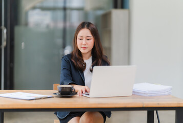 Focused Professional Grace: A young Asian businesswoman, radiating confidence and poise, diligently works on her laptop in a modern office setting. 