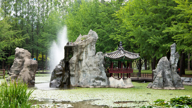 Nami Island, Chuncheon-si, Gangwon-do, South Korea - August 5, 2019: Fountain and a pavilion on pond with Nami Dodamsambong Peaks in summer