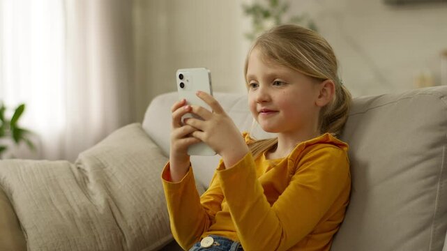 Little European girl user mobile phone smartphone cellphone online child chat networking browser internet electronic gadget device technology cyberspace daughter sofa connection website kid pupil home