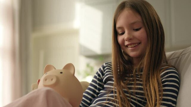 Happy little girl child kid daughter putting coins pennies in piggy bank money savings finance wealth business cash economy investing currency smiling success deposit budget income pay pig moneybox