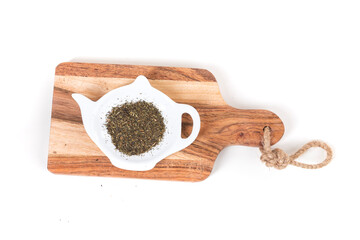 White glass teapot shaped dish and loose tea on a small wooden cutting board