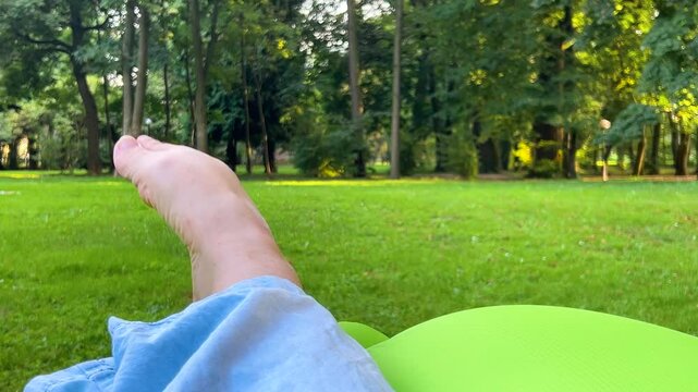 A woman wiggles her bare toes against the background of green grass in a summer park. Outdoor recreation.