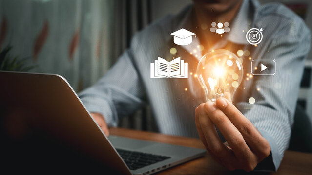 E-library concept. Businessman hold light bulb with virtual Ebook icons for electronic books online, knowledge base on internet, digital library or e-library.