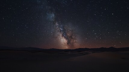 Fototapeta premium A panoramic shot of the desert under a starry night sky, with the Milky Way visible above the dark, quiet landscape.