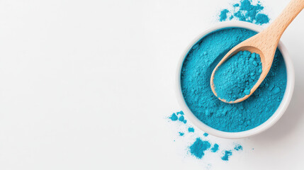 Bright blue spirulina powdered pigment in a white bowl with a wooden spoon, creating an artistic and colorful display on a clean background