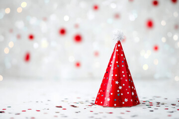A red party hat with polka dots is surrounded by colorful confetti and streamers.