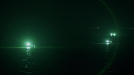 Boats fishing at night with green lights glowing on the dark water under a starless sky