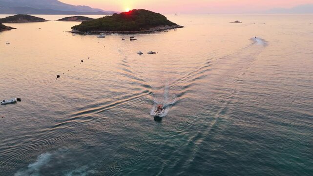 Boats speeding through calm waters near Ksamil, Albania at sunset with scenic islands in view