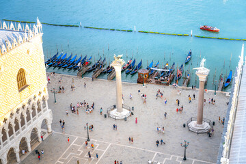 This aerial perspective showcases the vibrant Piazetta San Marco in Venice, featuring historic columns, bustling crowds, and traditional gondolas along the waterfront.