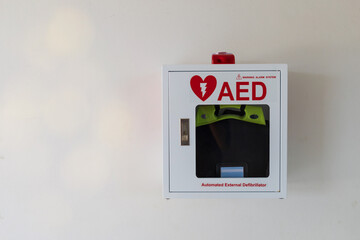 Automated External Defibrillator medical first aid device on white wall. Portable electronic device...