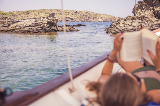 Young girl reading a book while relaxing on a boat in the Mediterranean