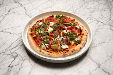 Italian Prosciutto pizza. Pizza with fresh tomatoes, rucola, ham on white plate.